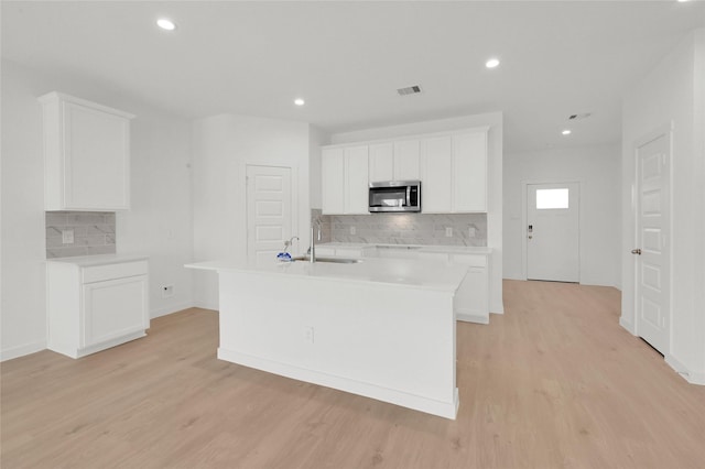 kitchen featuring stainless steel microwave, a sink, backsplash, light countertops, and light wood-style flooring