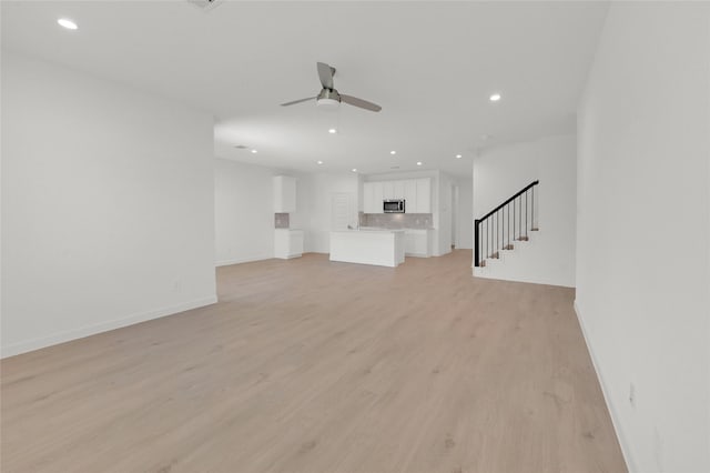 unfurnished living room featuring recessed lighting, light wood-type flooring, a ceiling fan, baseboards, and stairway