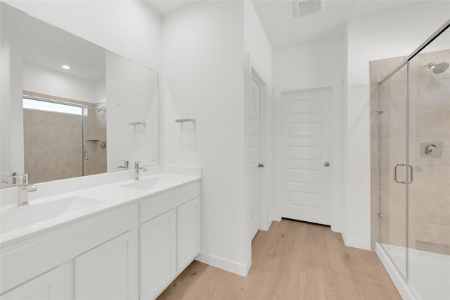 bathroom with wood finished floors, a shower stall, double vanity, and baseboards