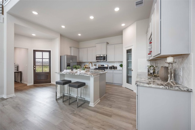 16809 Needlepoint Dr, Conroe, TX 77302 - kitchen featuring appliances with stainless steel finishes, light wood-type flooring, a center island with sink, tasteful backsplash, and a sink