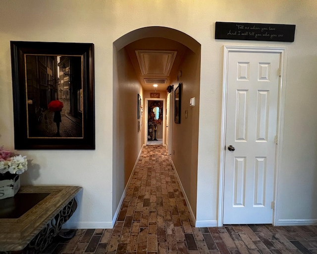 corridor featuring arched walkways, baseboards, and brick patterned flooring