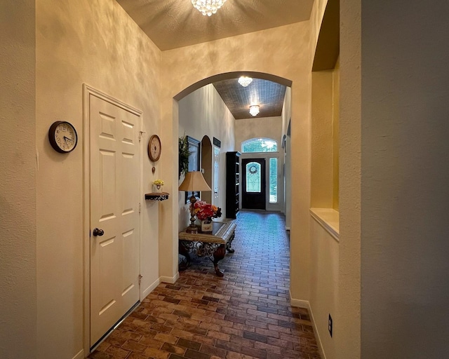 3002 Sandleigh Dr, Spring, TX 77388 - corridor featuring arched walkways, a textured wall, brick floors, baseboards, and a chandelier