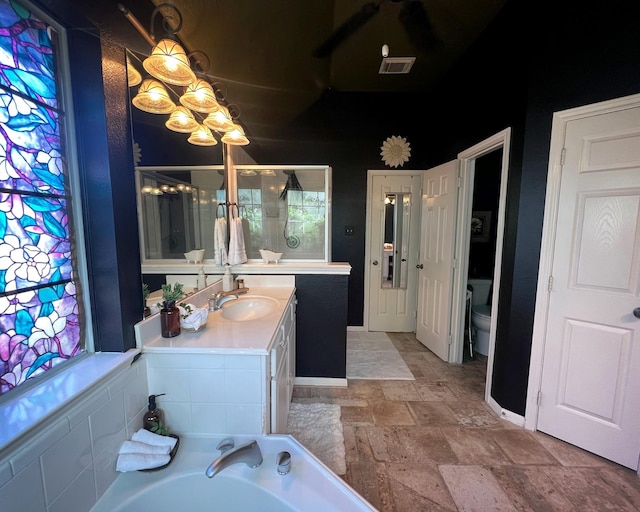 bathroom with stone tile floors, vanity, baseboards, toilet, and a stall shower