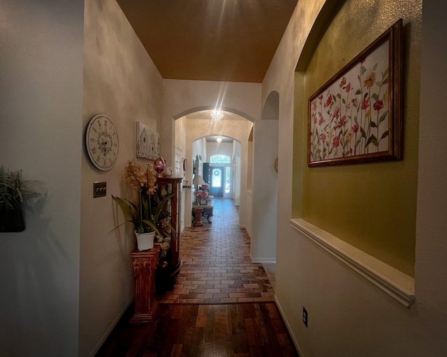 hallway featuring arched walkways, brick floors, and baseboards