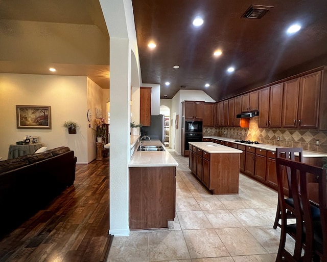 kitchen with black appliances, a sink, under cabinet range hood, vaulted ceiling, and decorative backsplash