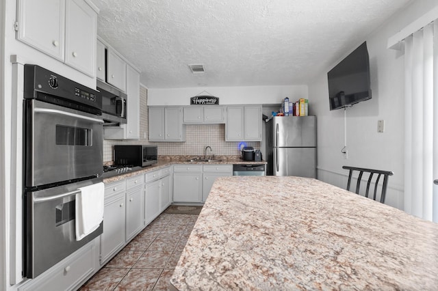4914 Airport Blvd, Houston, TX 77048 - kitchen featuring stainless steel appliances, a sink, backsplash, a textured ceiling, and light tile patterned flooring