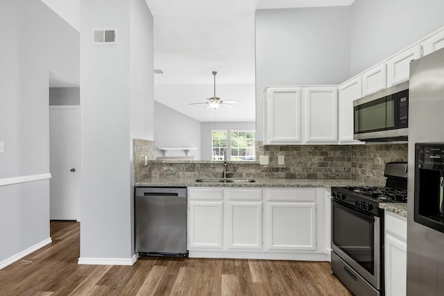 kitchen with appliances with stainless steel finishes, a sink, wood finished floors, white cabinets, and light stone countertops