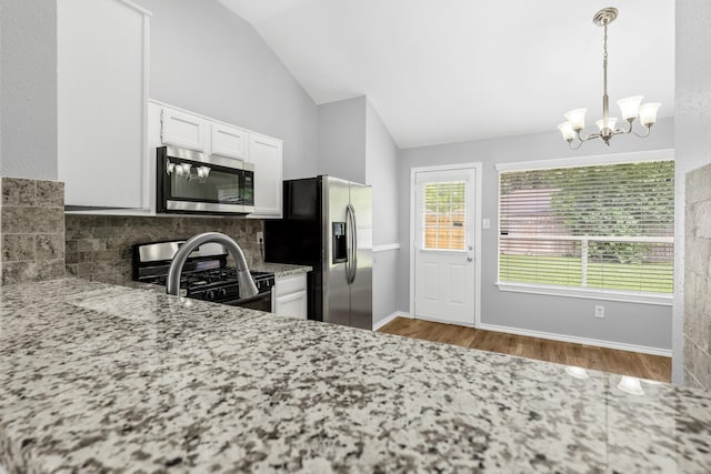kitchen with stainless steel appliances, vaulted ceiling, backsplash, wood finished floors, and a chandelier
