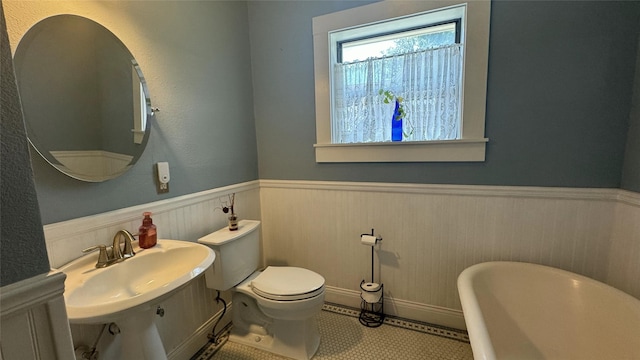 bathroom with wainscoting, a soaking tub, toilet, and a sink
