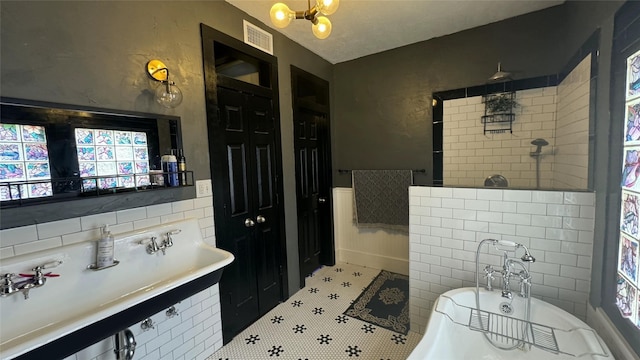 full bath with a freestanding bath, walk in shower, a chandelier, tile patterned floors, and wainscoting