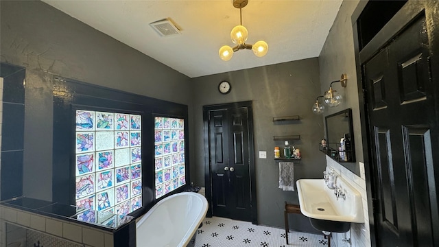 full bath featuring a freestanding bath, a chandelier, tile patterned flooring, and a sink