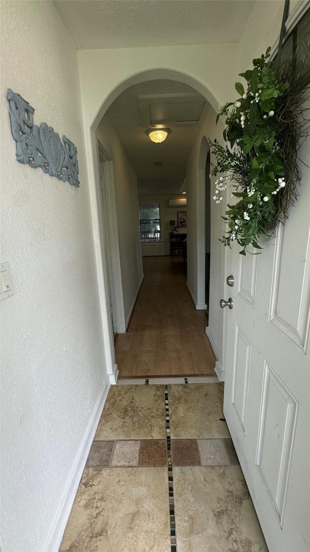 hall featuring arched walkways, baseboards, and stone finish floors