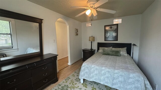bedroom featuring arched walkways, light wood-type flooring, and a ceiling fan