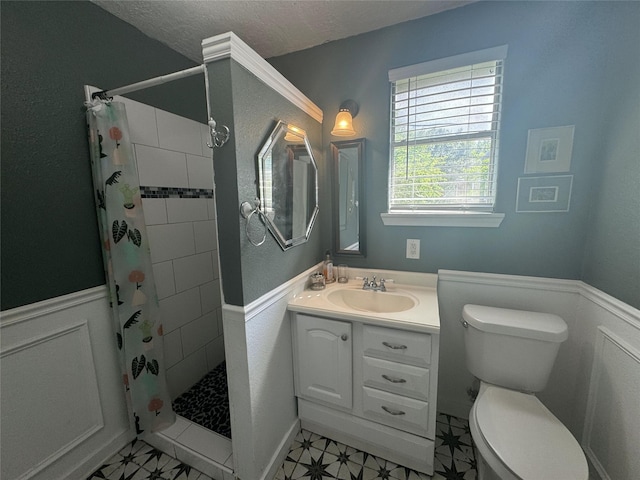 bathroom with a tile shower, vanity, toilet, wainscoting, and a textured ceiling