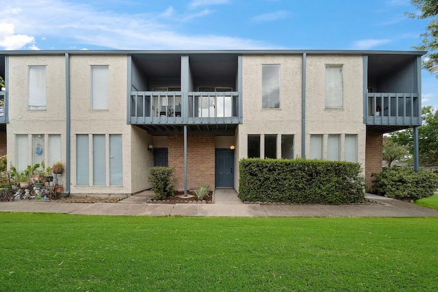 back of house with a balcony, stucco siding, a lawn, and brick siding