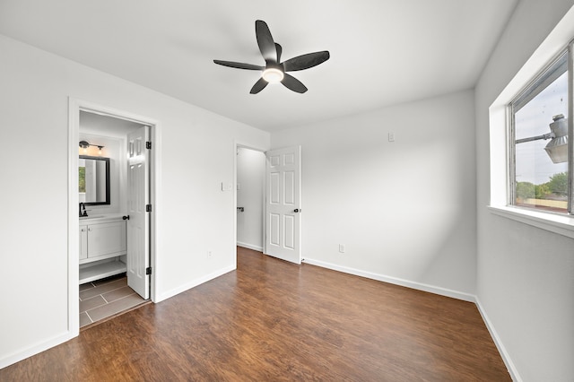 unfurnished bedroom featuring wood finished floors, baseboards, ensuite bath, and a ceiling fan