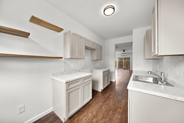 kitchen featuring a sink, tasteful backsplash, dark wood-style flooring, gray cabinetry, and light stone countertops