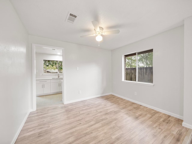 empty room with ceiling fan, plenty of natural light, and light wood-style floors