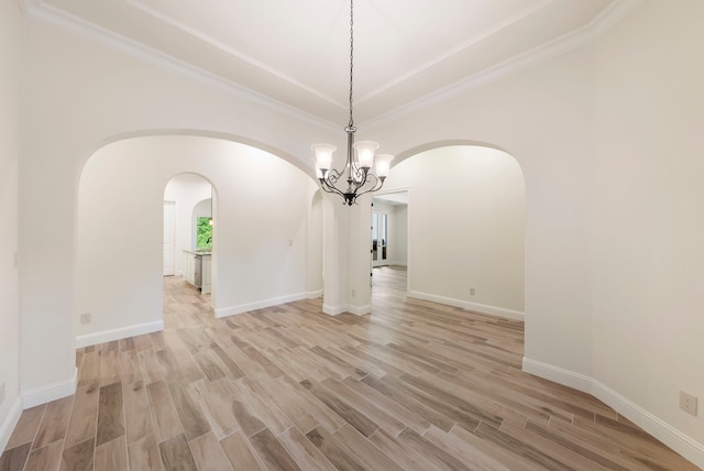 unfurnished dining area with arched walkways, a chandelier, light wood finished floors, and baseboards