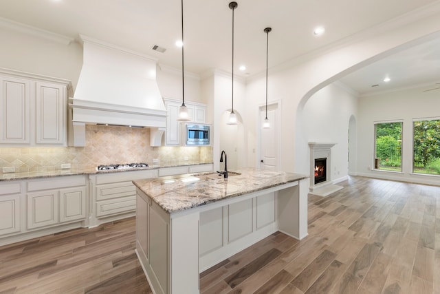 kitchen with a sink, custom exhaust hood, stainless steel microwave, white gas stovetop, and decorative backsplash