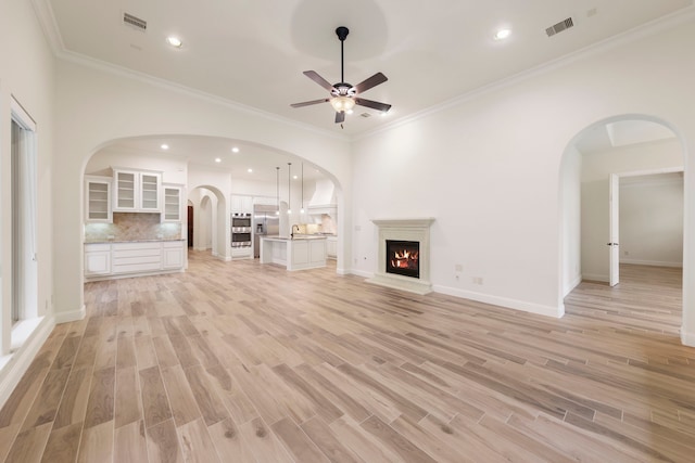 unfurnished living room with arched walkways, a ceiling fan, light wood-style floors, a warm lit fireplace, and recessed lighting