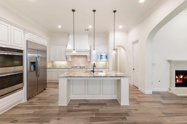kitchen featuring built in appliances, premium range hood, light wood finished floors, a sink, and crown molding