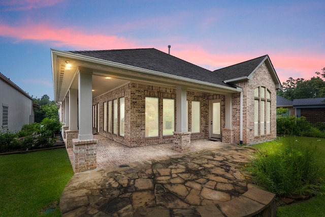 rear view of property featuring brick siding, roof with shingles, a patio area, and a yard