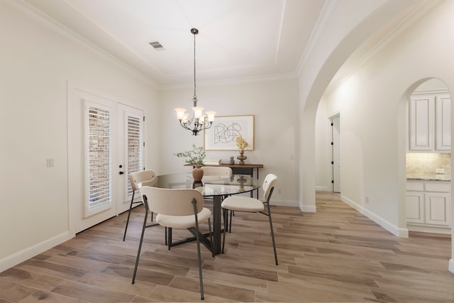 dining room with light wood-style flooring, arched walkways, a chandelier, baseboards, and ornamental molding