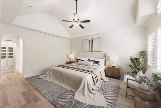 bedroom with vaulted ceiling, arched walkways, light wood-style floors, a ceiling fan, and ornamental molding