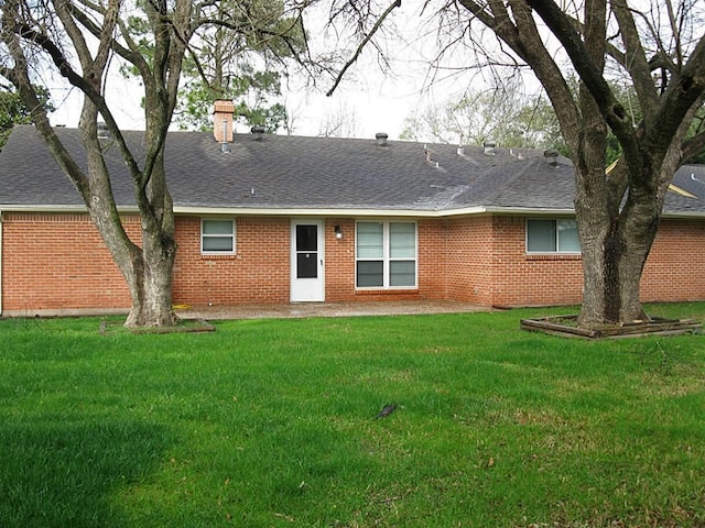rear view of property with brick siding, roof with shingles, a lawn, and a chimney