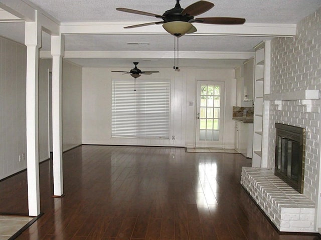 unfurnished living room featuring ceiling fan, wood finished floors, a brick fireplace, a textured ceiling, and beam ceiling