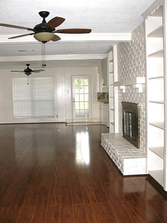 unfurnished living room featuring a ceiling fan, wood finished floors, a textured ceiling, a brick fireplace, and beamed ceiling