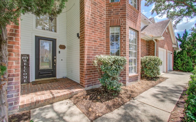 property entrance with brick siding, a shingled roof, an attached garage, and driveway