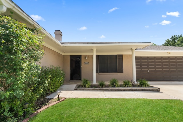 view of exterior entry featuring an attached garage, a chimney, concrete driveway, and a lawn