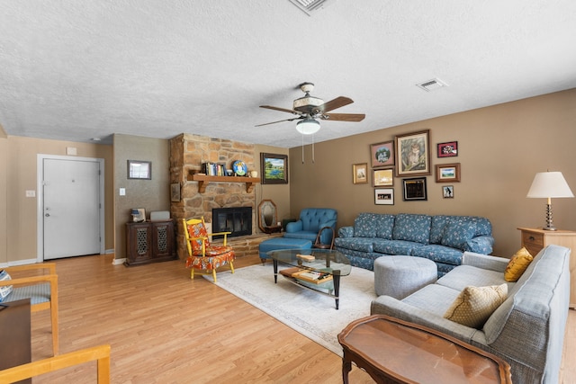 living room with a textured ceiling, light wood-style floors, a ceiling fan, and a stone fireplace