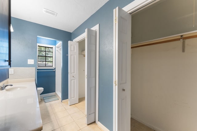 bathroom featuring toilet, tile patterned flooring, vanity, baseboards, and a shower