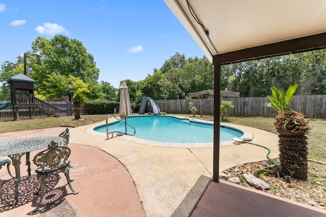 view of swimming pool with a water slide, a patio area, a fenced backyard, and a playground