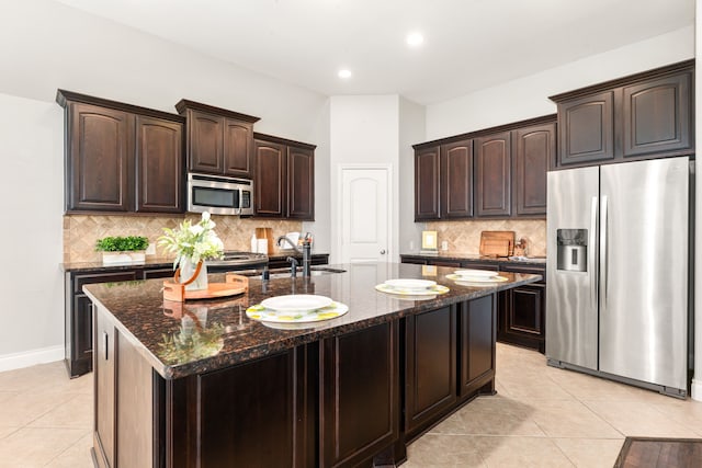 2314 Laurel Loch Ln, Pearland, TX 77584 - kitchen featuring appliances with stainless steel finishes, light tile patterned floors, dark stone countertops, dark brown cabinets, and tasteful backsplash