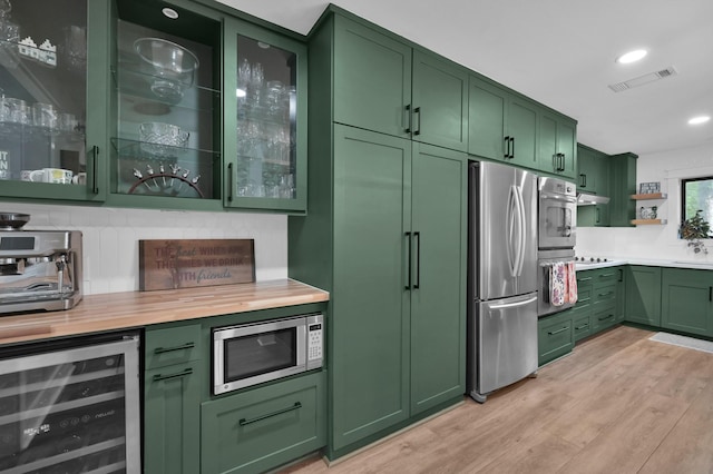914 Rustic Oaks Dr, Magnolia, TX 77354 - kitchen with green cabinetry, stainless steel appliances, wine cooler, under cabinet range hood, and light wood-style flooring