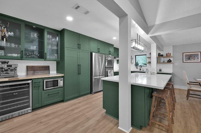 914 Rustic Oaks Dr, Magnolia, TX 77354 - kitchen featuring green cabinetry, wine cooler, appliances with stainless steel finishes, light countertops, and light wood-style flooring