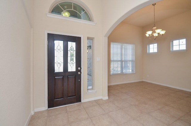 entrance foyer with a chandelier, arched walkways, light tile patterned floors, a towering ceiling, and baseboards