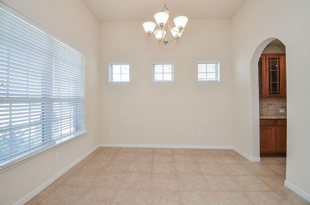 unfurnished dining area featuring arched walkways, a chandelier, and baseboards