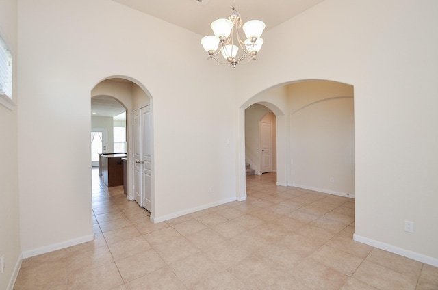 empty room with arched walkways, a chandelier, light tile patterned floors, a towering ceiling, and baseboards