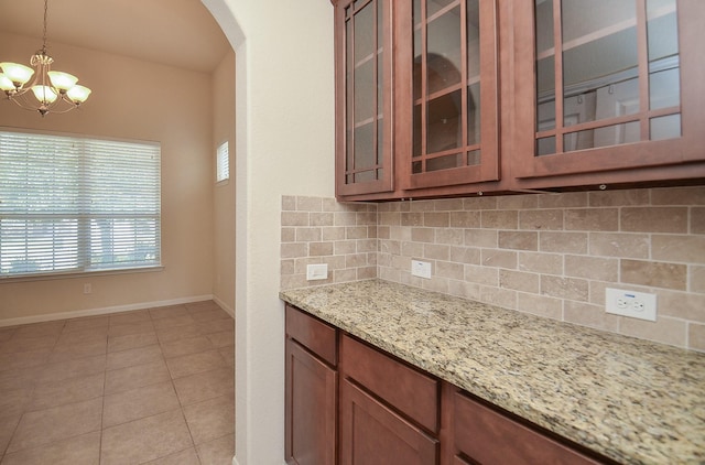 kitchen featuring decorative backsplash, arched walkways, a chandelier, pendant lighting, and light stone countertops