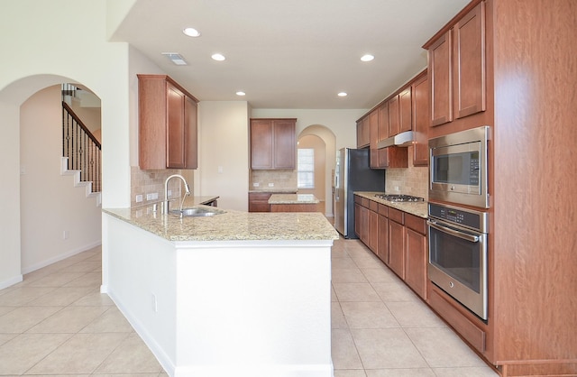 kitchen featuring stainless steel appliances, a sink, a peninsula, light tile patterned flooring, and backsplash