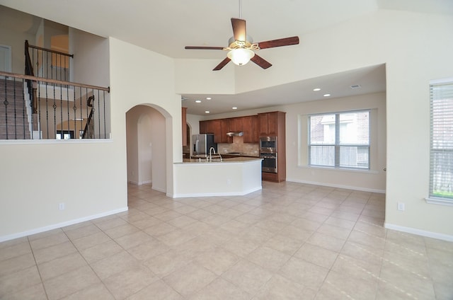 unfurnished living room with arched walkways, ceiling fan, high vaulted ceiling, a sink, and recessed lighting