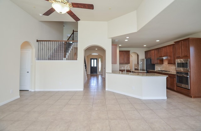 kitchen featuring stainless steel appliances, a ceiling fan, under cabinet range hood, decorative backsplash, and a sink