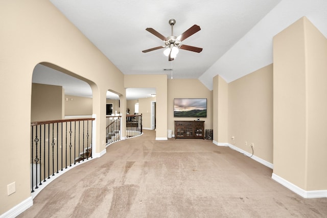 unfurnished living room with ceiling fan, carpet flooring, baseboards, vaulted ceiling, and arched walkways