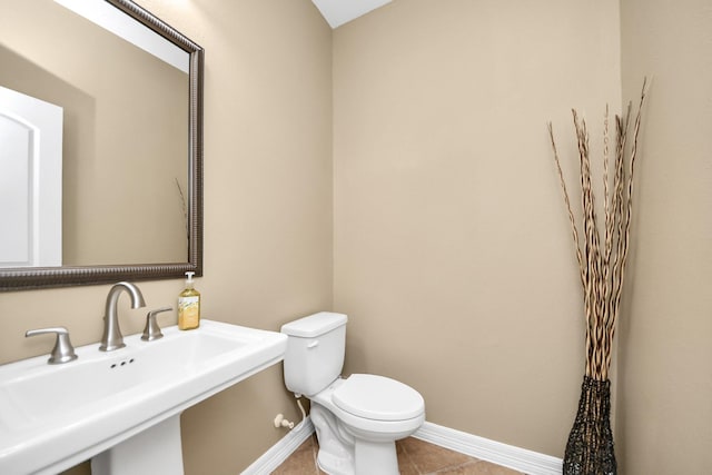 half bath with a sink, toilet, baseboards, and tile patterned flooring