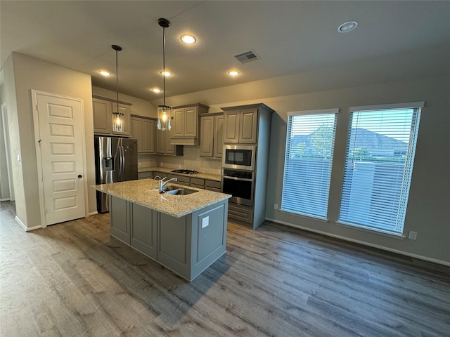 kitchen with appliances with stainless steel finishes, wood finished floors, a center island with sink, backsplash, and recessed lighting